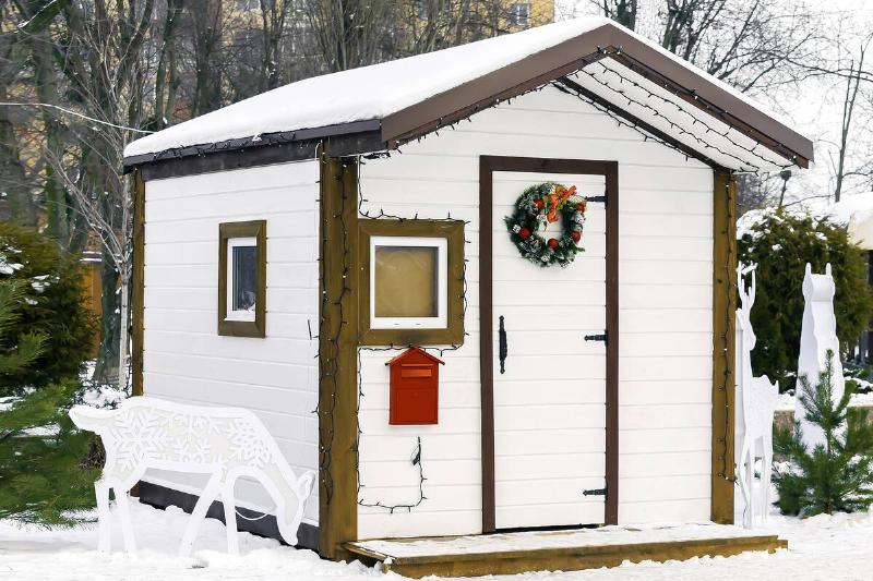 White wooden house of Santa Claus artificial structure with red post mail box for letters from kids children in winter snowy city park. Christmas xmas new year holiday concept.