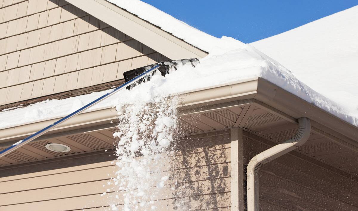 Someone using a specialized shovel to scrape snow off their roof.