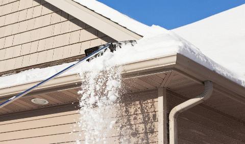Someone using a specialized shovel to scrape snow off their roof.