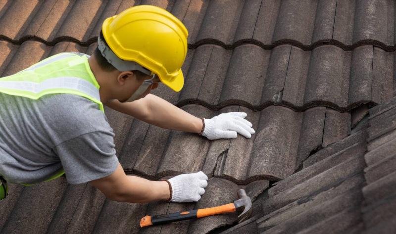 A close shot of a worker on a roof fixing a cracked shingle.
