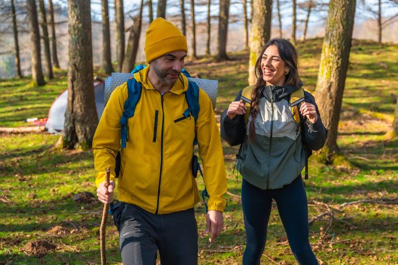 Happy hikers walking in forest, carrying backpacks and using hiking poles, enjoying nature near their campsite