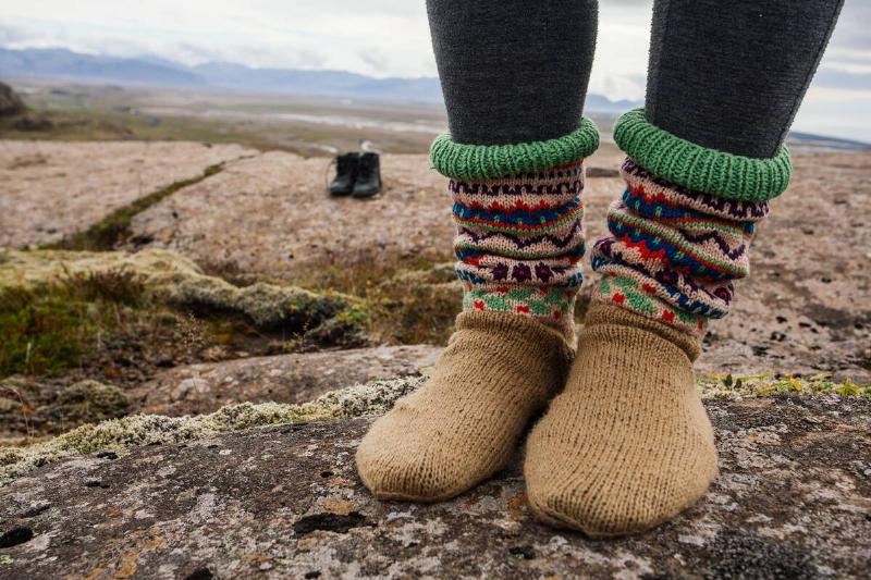 A person standing on a large flat rock, boots off, showing their knit socks.