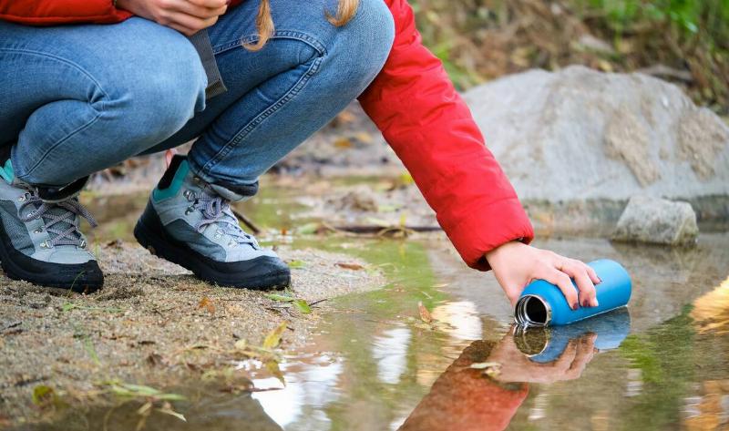 A woman filling her water bottle in a stream.