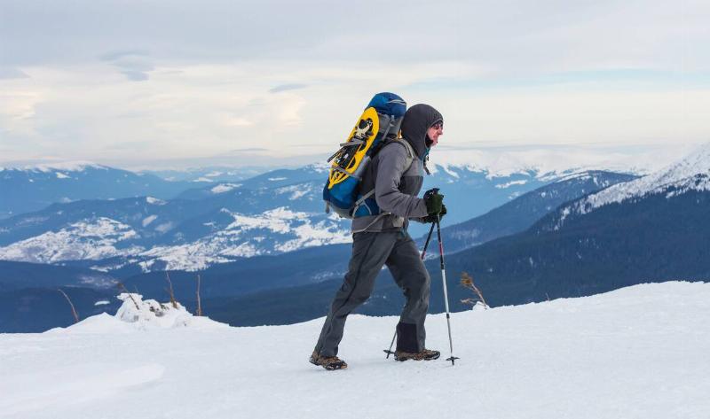 A man hiking through the snow with a hiking backpack and ski poles.