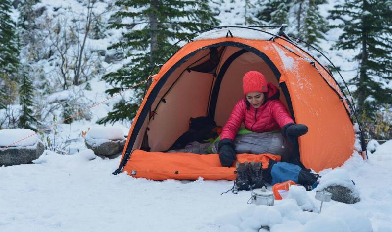 A woman in her open tent in the snow, looking through her hiking pack.
