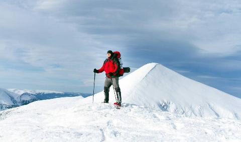 A man hiking through the snow with a hiking backpack and ski poles.