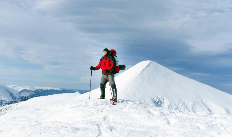 A man hiking through the snow with a hiking backpack and ski poles.