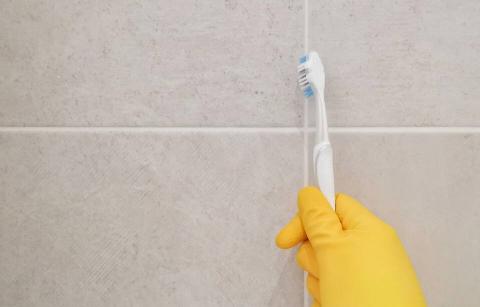 A hand in a glove cleaning grout with a toothbrush.