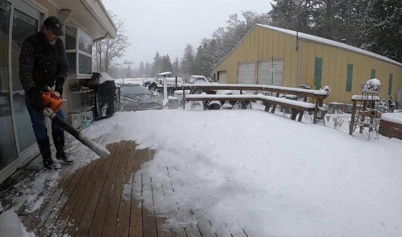 A man using a leafblower to blow snow off his porch.