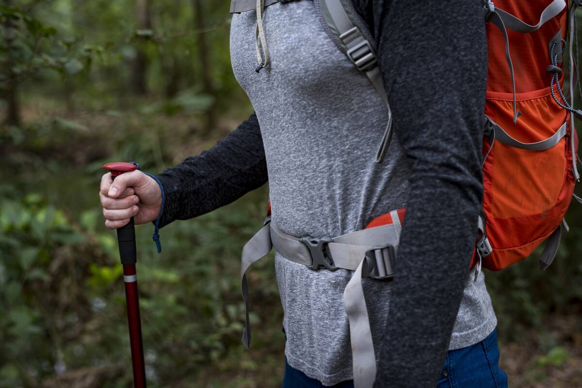 A person hiking in a forest, close view of their backpack straps.