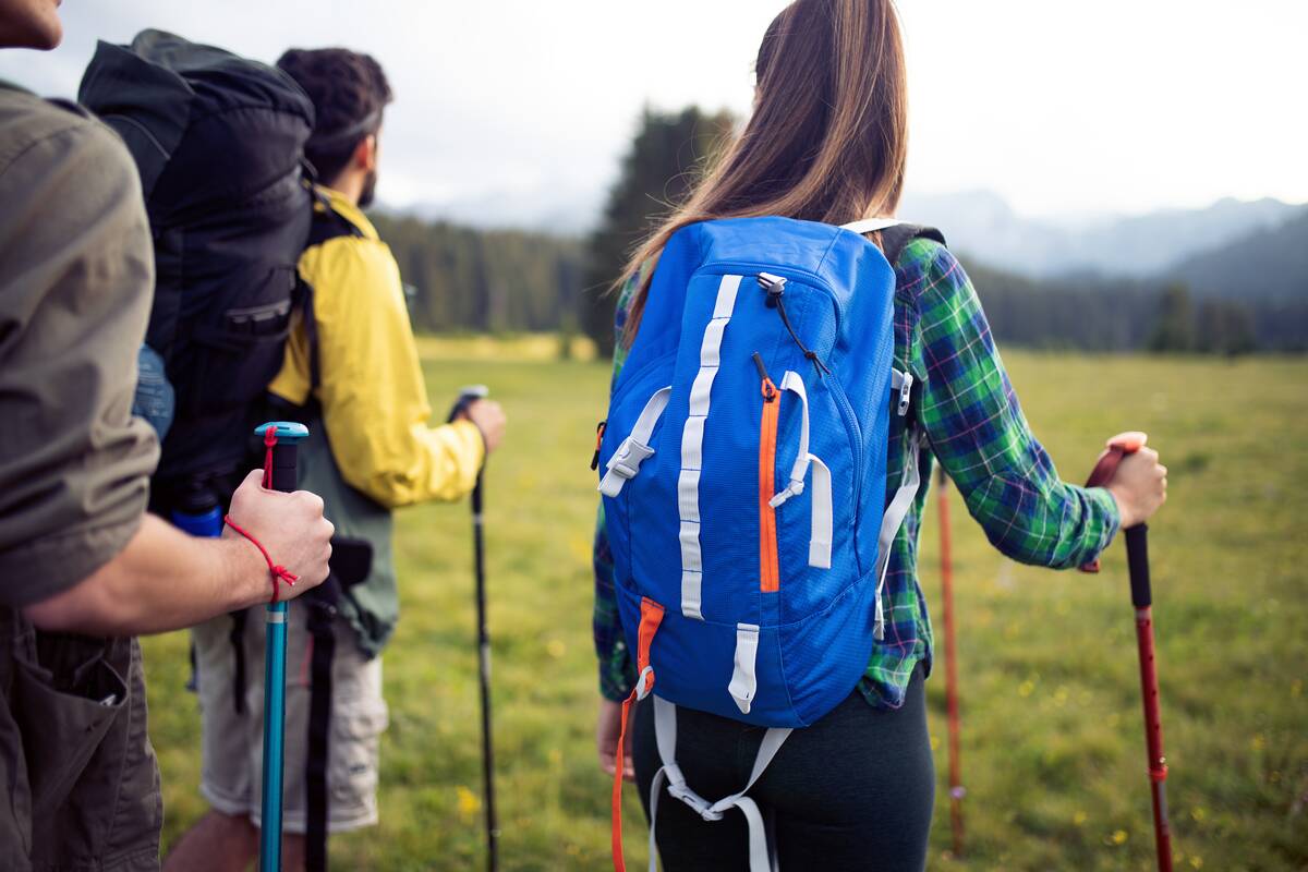 A group of hikers, focus on one woman's backpack that's bright blue with reflective white straps.