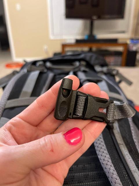 A person holding up a built-in whistle fixed to their backpack clasp.