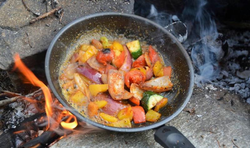 Someone cooking food in a pan over a fire.