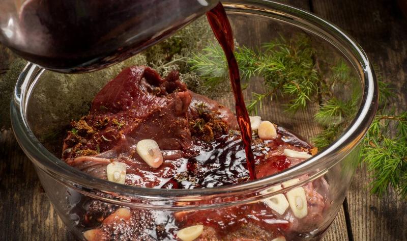 Someone pouring marinade over meat in a bowl.