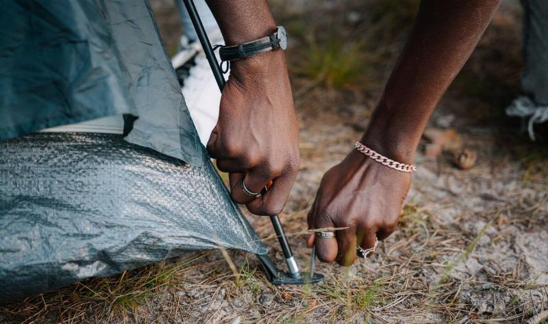 A close photo of someoen putting an anchor in the ground for a tent.