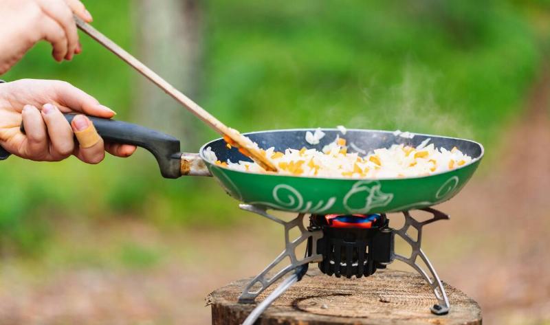 A person sauteing vegetables in a pan on a camp stove.