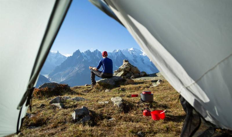 A man sitting outside of his tent in the mountains.