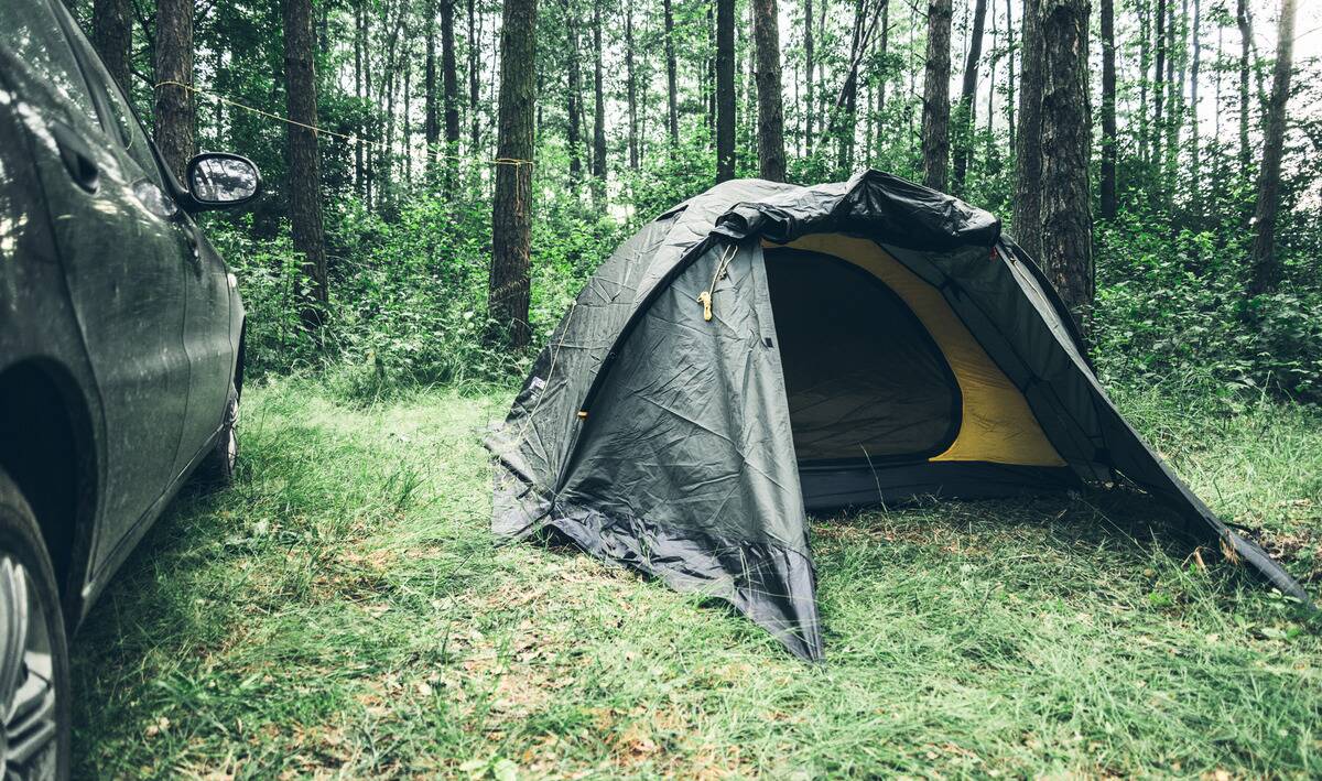 A tent set up right next to a car.