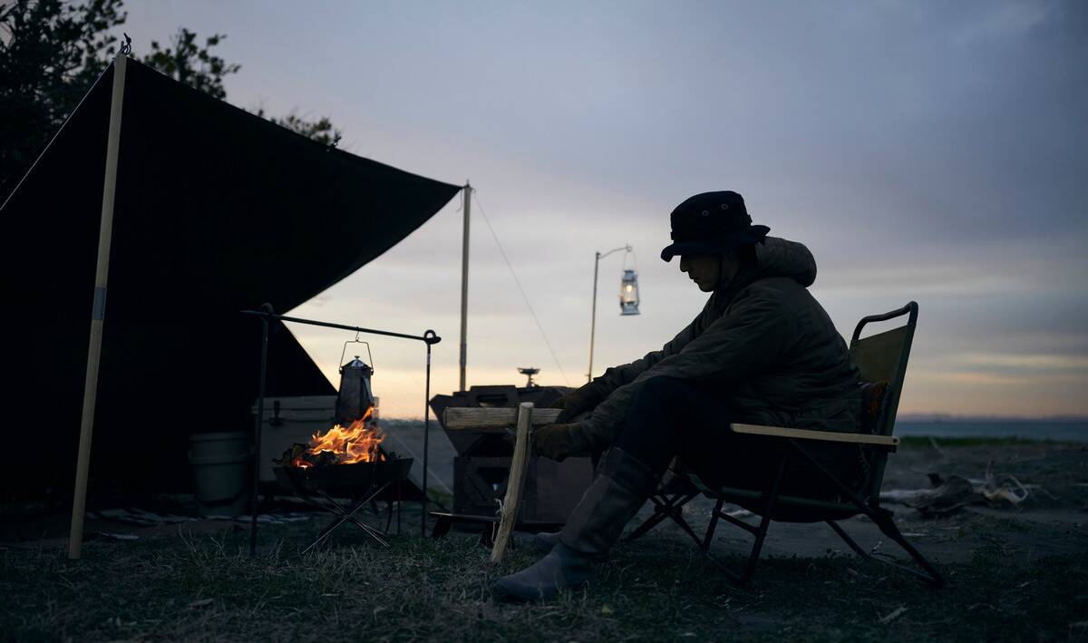 A person sitting outside of a leanto at dusk.