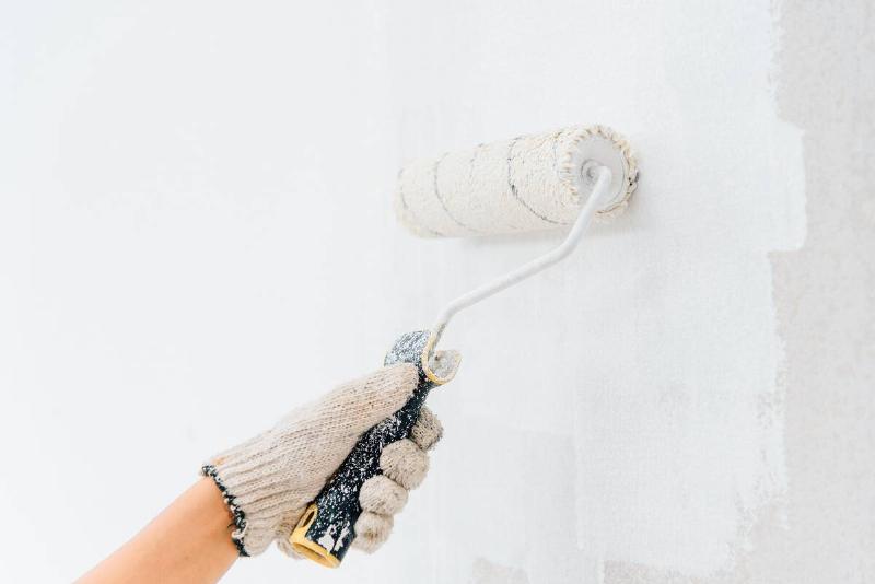 Hands young woman painting the walls with a roller using white paint.