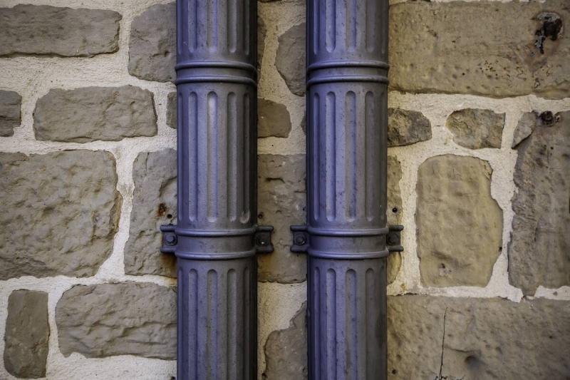 Two iron pipes attached to a stone wall.