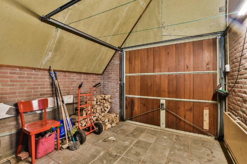 Spacious garage with closed door and garden tools to take care of garden and washing machine