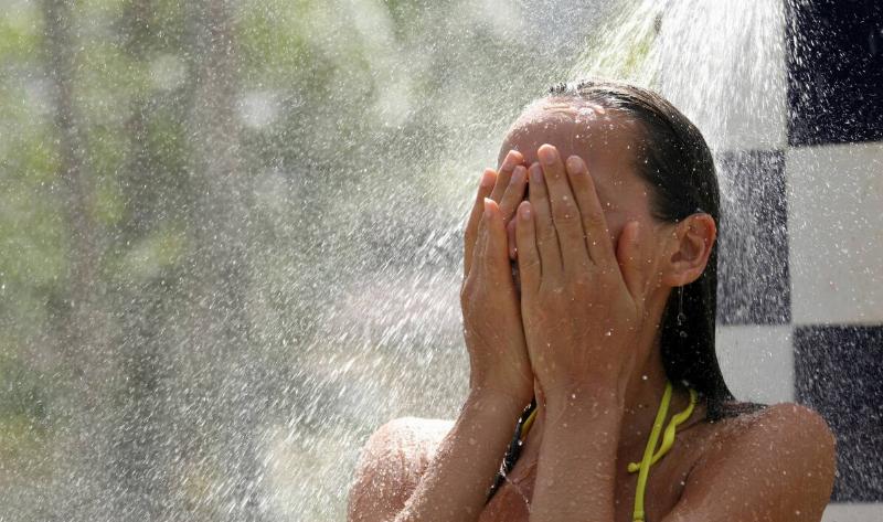 A woman covering her face with her hands under an outdoor shower head.