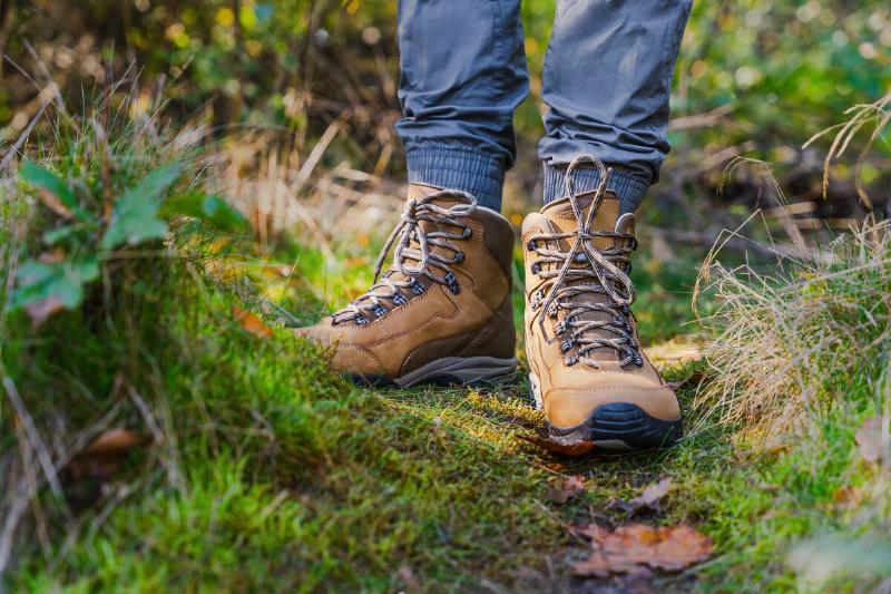Hiker in brown trekking boots with tied stand on mossy hiking trail in forest