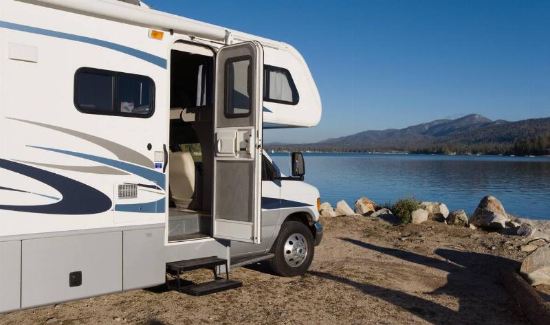 An RV parked next to a lake, the door open.