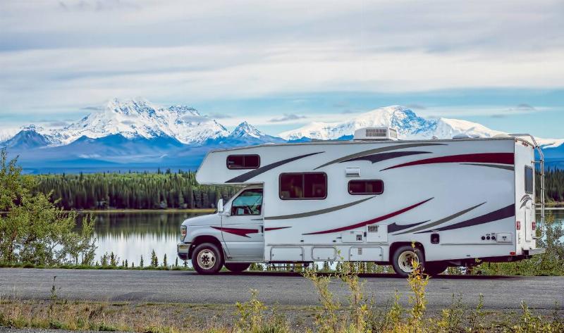 An RV parked next to a lake, the door open.