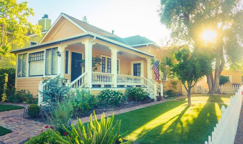 A home in the summer, the sun shining on it, the lawn and plants around it all bright green.