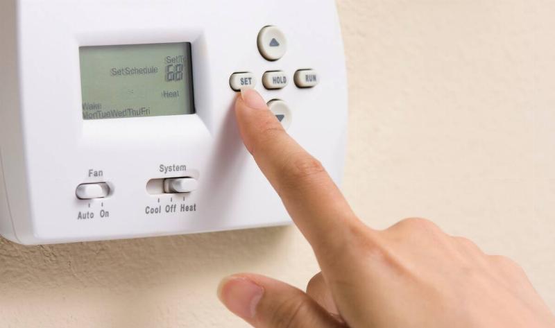 A hand pressing a thermostat button.