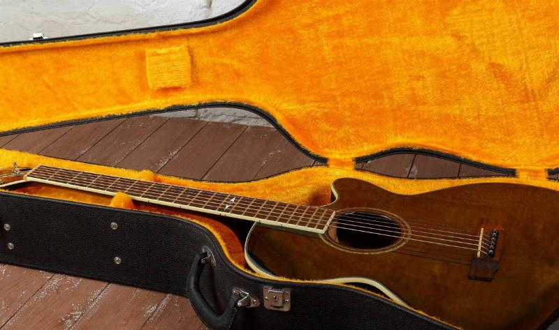 An open hard guitar case with orange velvet inside, as well as a brown acoustic guitar.