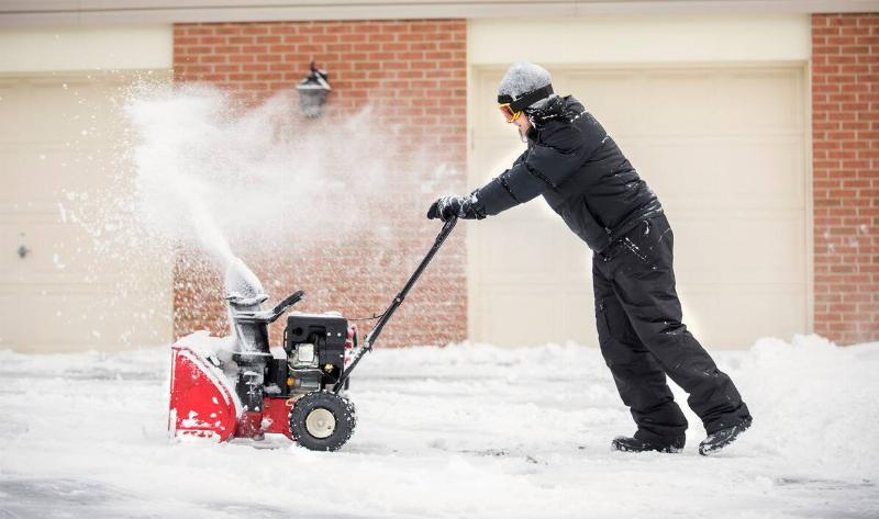 A man pushing a gas snowblower.