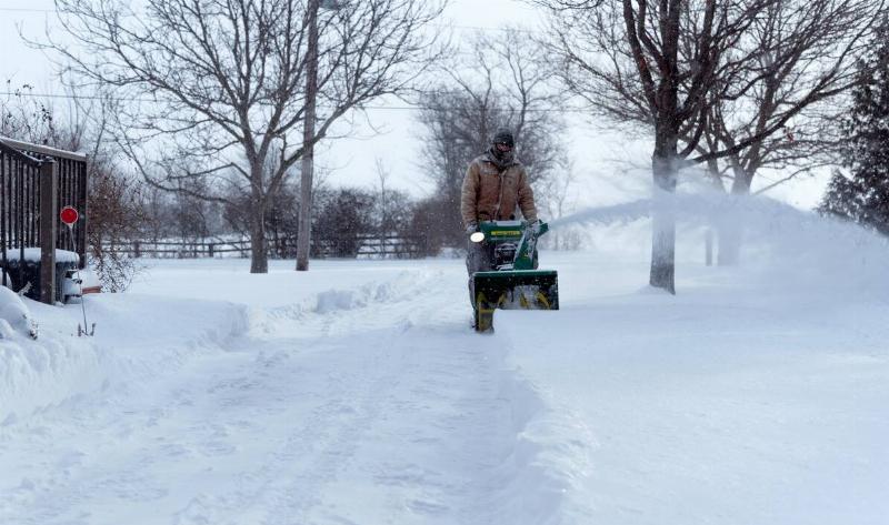 A man pushing a snowblower through tall snow.
