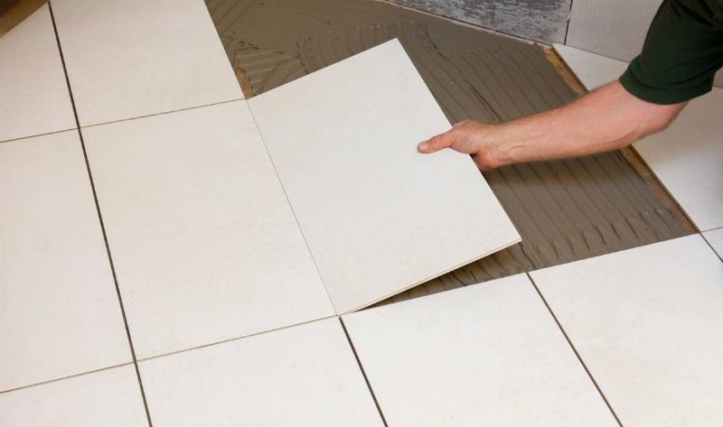 A person laying down a flooring tile.
