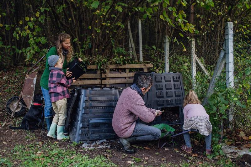 Family removing compost from a composter in garden, and also composting  kitchen waste in composter. Concept of composting and sustainable 
organic gardening.