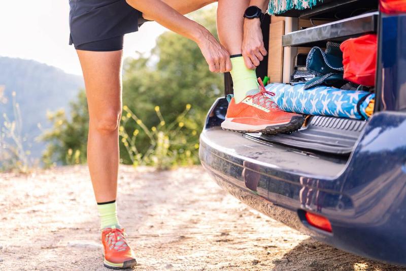 cropped photo of an unrecognizable woman in a camper van preparing to trail running and do sports in nature, concept of outdoor activities and healthy lifestyle