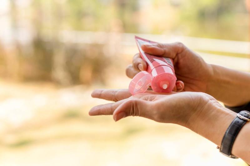 A person squeezing a small amount of hand cream into their hand from a small bottle.