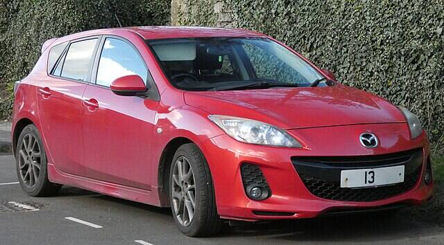 Red 2013 Mazda 3 parked next to a building