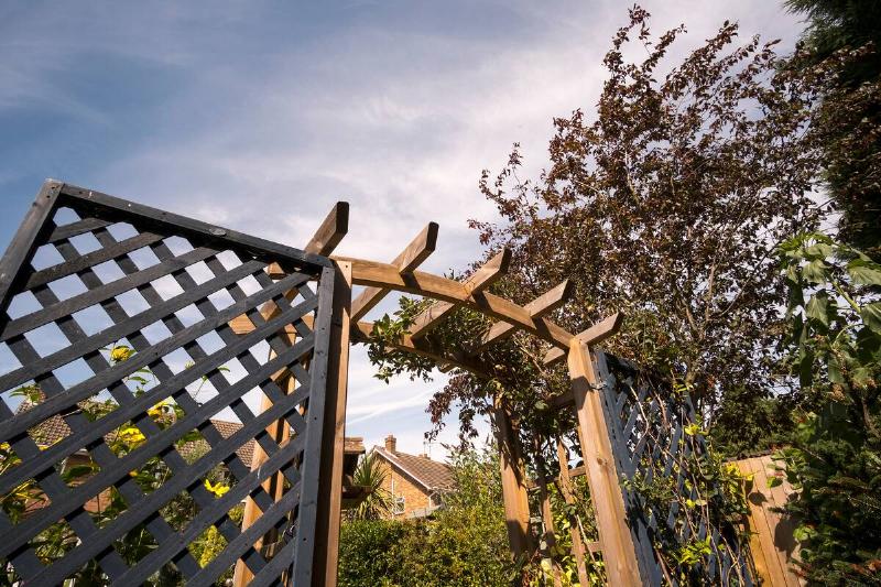 A low-angle photo of a wood arbor with lattice fence on either side.