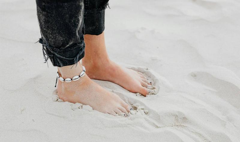 A person standing in sand with bare feet.