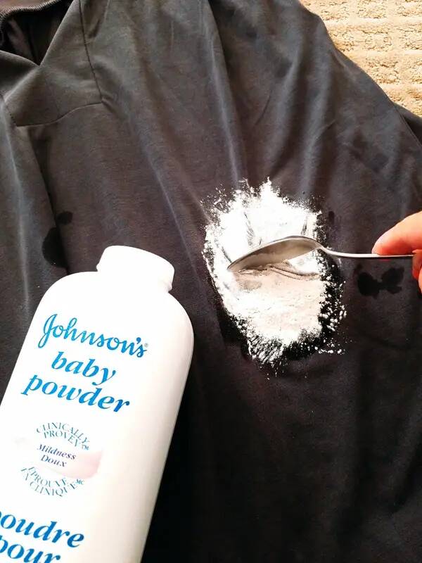 A person spreading baby powder on a grease stain on a shirt.