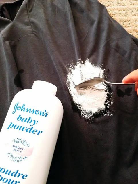 A person spreading baby powder on a grease stain on a shirt.