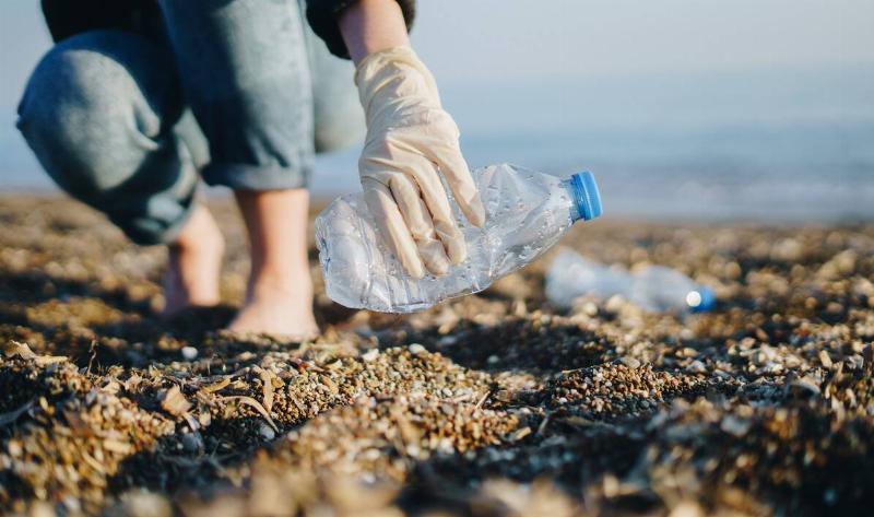 A person picking up a plastic bottle off a beach.