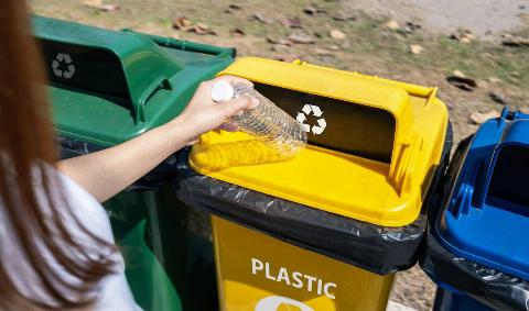 A person putting a plastic bottle in a recycling bin.