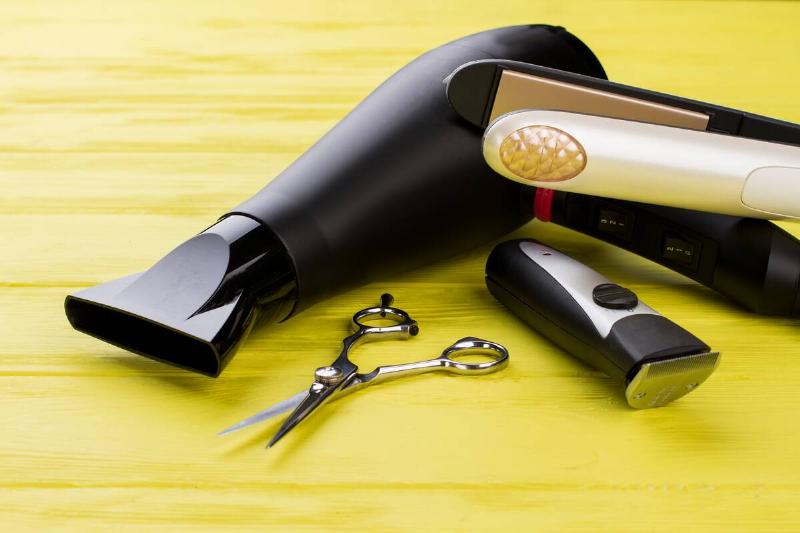 Hairdresser tools on color background. Hair dryer, hair sraightener, scissors and electric trimmer on wooden background.