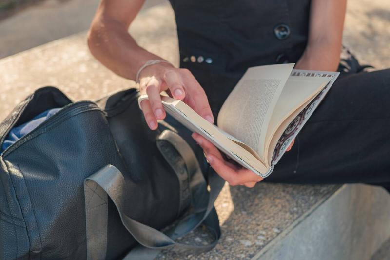 Close-up of a young fashionable man in black clothes reading a book in a park