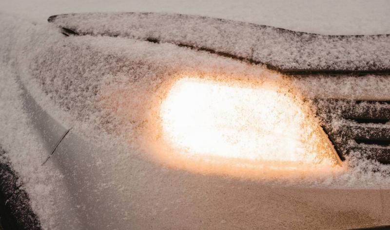 A car headlight, on but covered in snow.
