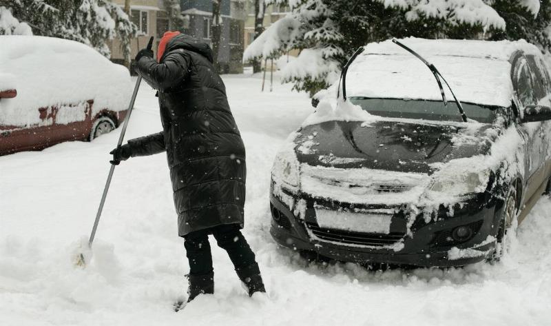 A woman clearing snow around her car.